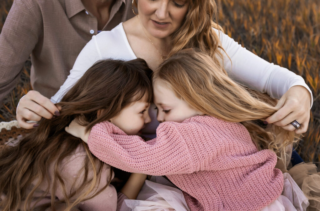 Mom with two little girls snuggling on her lap. Mom is playing with their hair.