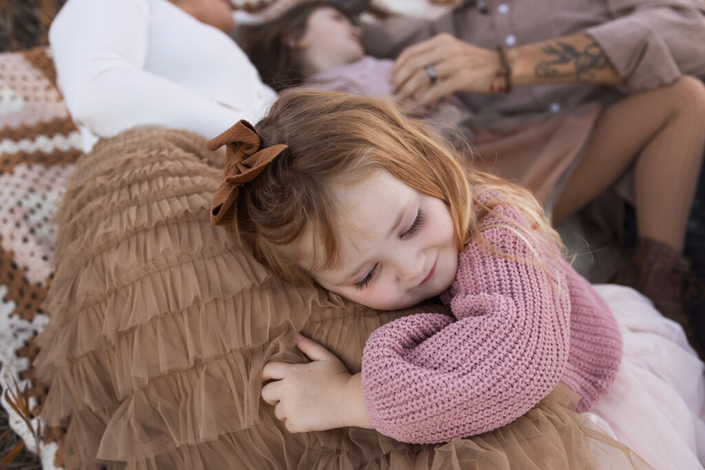 Little girl snuggling on her mom's leg on a blanket.