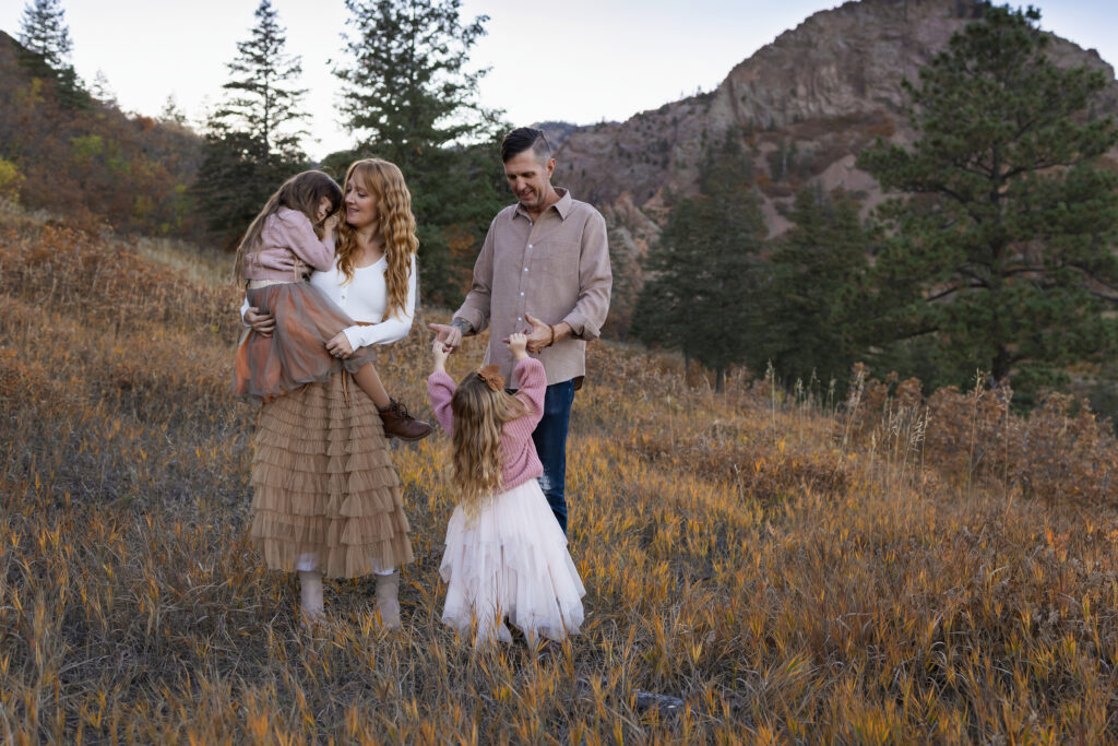 Mom and dad of two girls standing in orange grass with a mountain backdrop.