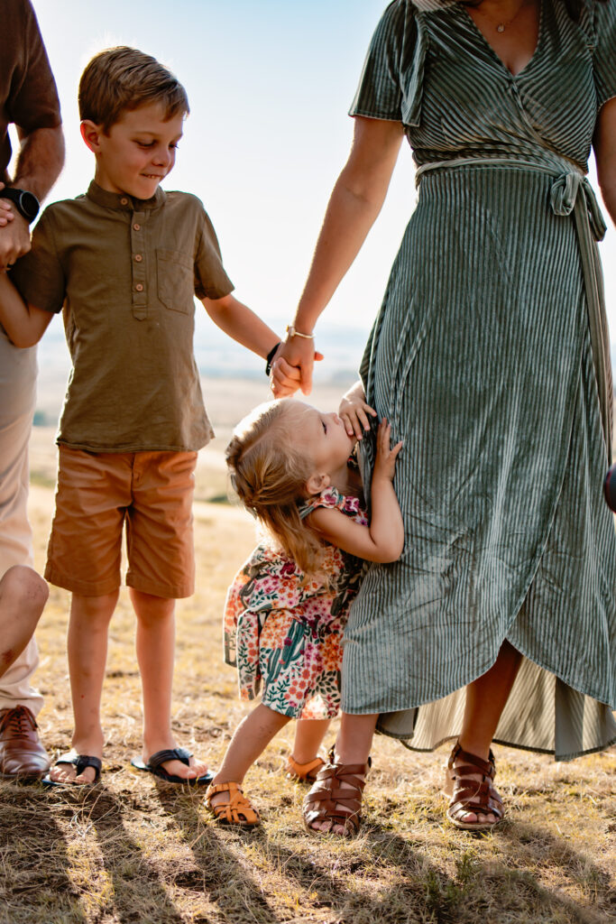 Little girl holding onto her mom's leg and mom holding her son's hand.