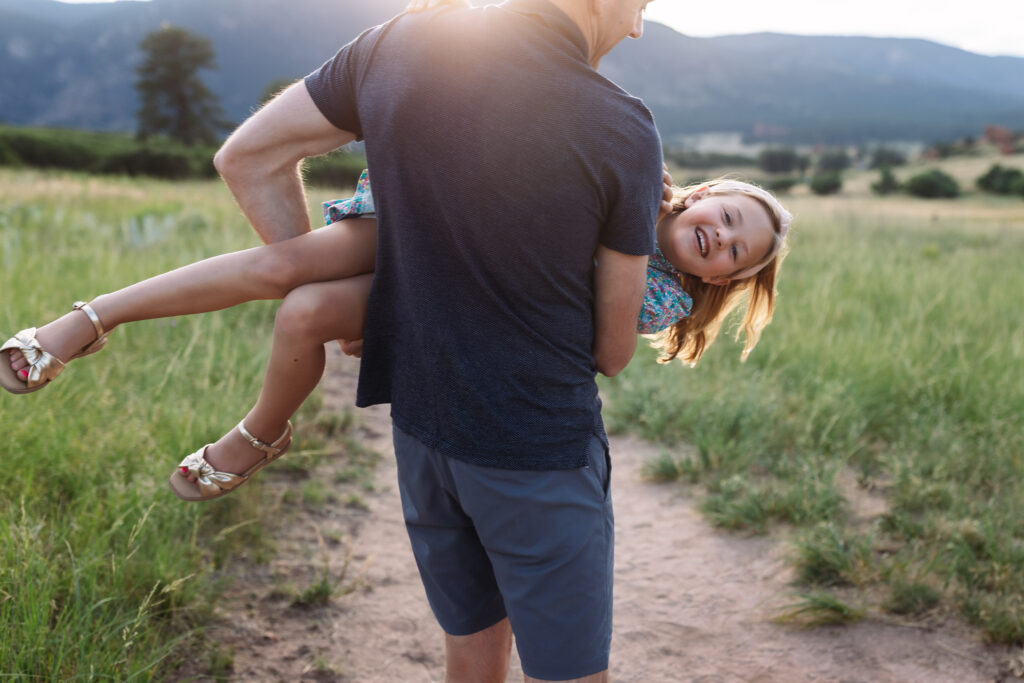 Little girl being carried by her dad sideways with a big smile.