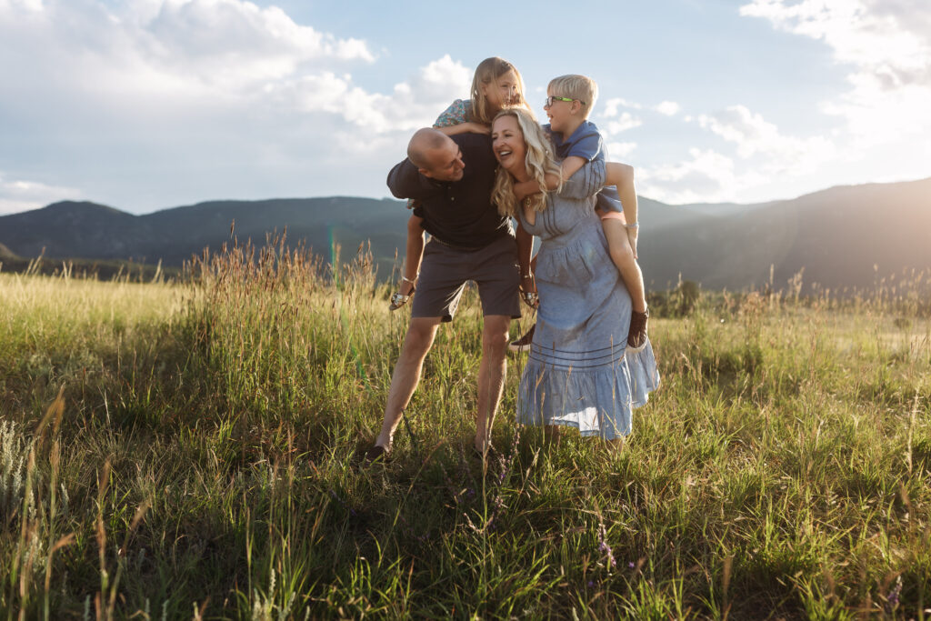 Family of four with kids on the parents' backs, laughing and having fun.