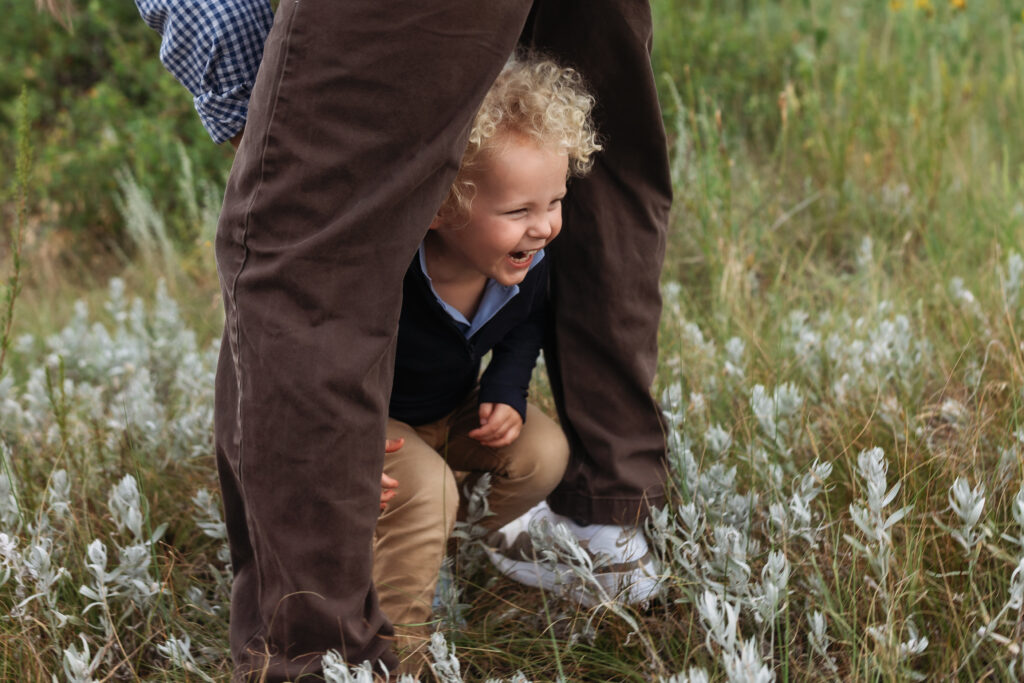 Toddler boy walking through his dad's legs.