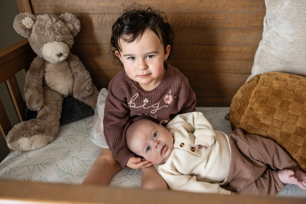 Big sister holds newborn baby brother in his crib near Colorado Springs, CO.