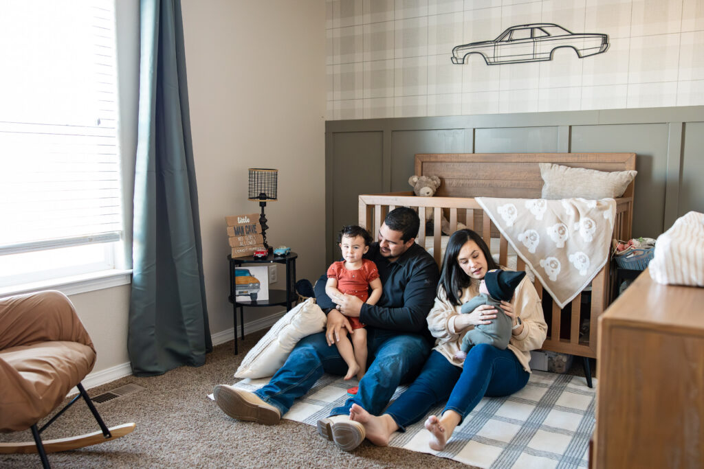 Family sits on the floor of a boys nursery at a newborn photoshoot outside of Colorado Springs.