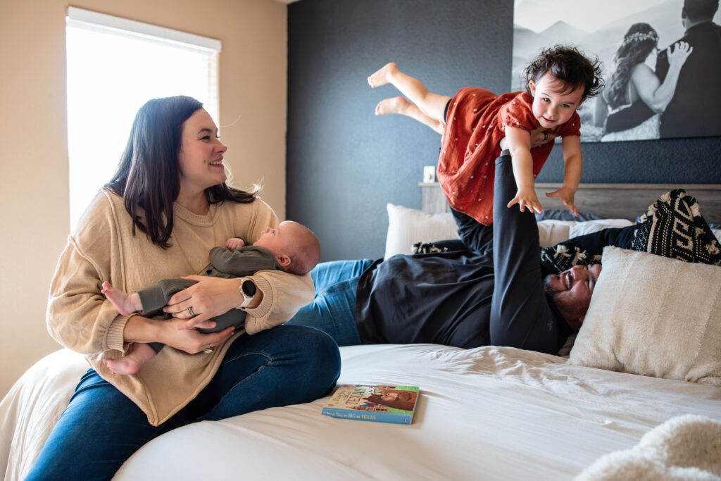 Family of four at a newborn photography session outside of Colorado Springs. Mom is holding newborn while dad flies toddler like an airplane.