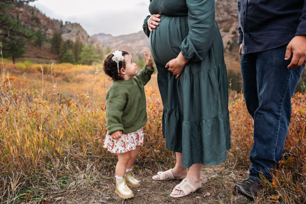 Maternity photo with young girl touching mom's belly taken in a beautiful location in Colorado Springs.