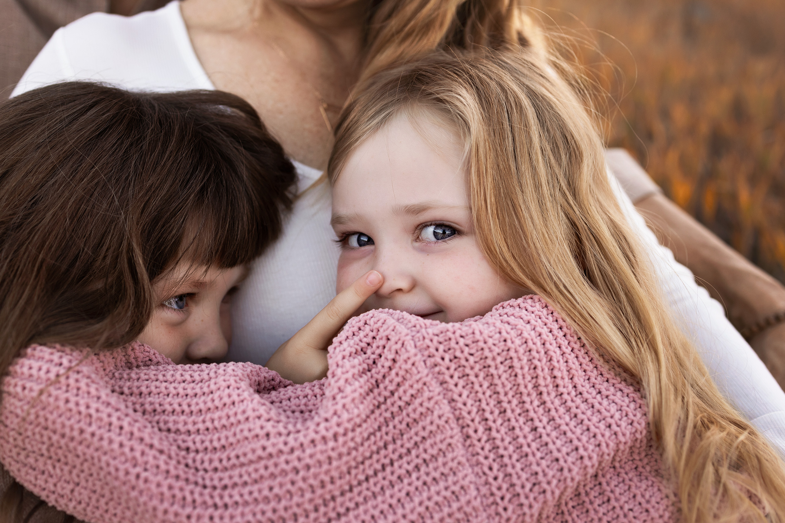Two sisters snuggle on their mom's lap during a lifestyle family session in Colorado Springs.