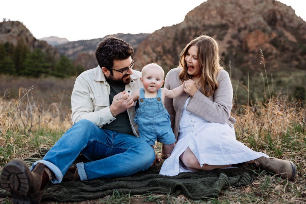 Mom and Dad have big smiles while they watch their baby try to stand at baby photo session in Colorado Springs.