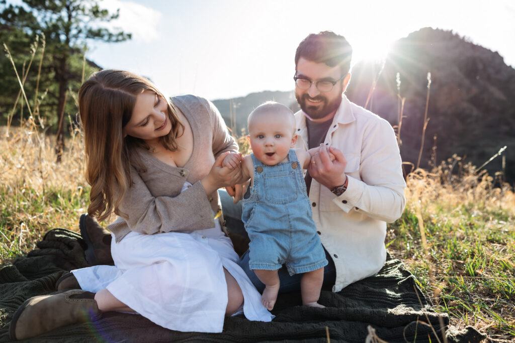Baby tries to stand while mom and dad hold his hands at baby photography session in Colorado Springs.