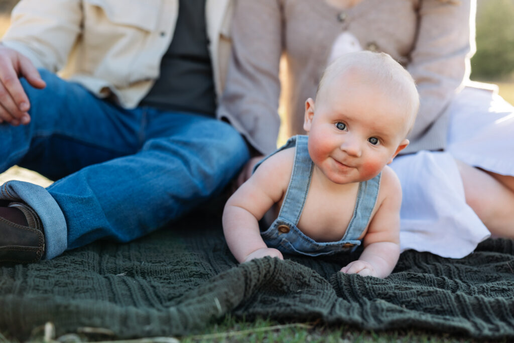 Six month old baby smiles at camera while laying on his stomach at a baby photo session in Colorado Springs.