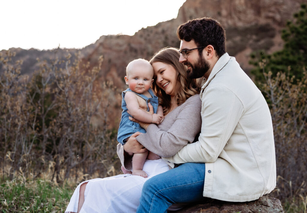 Mom and Dad sit on a rock holding their baby at a photography session in Colorado Springs.